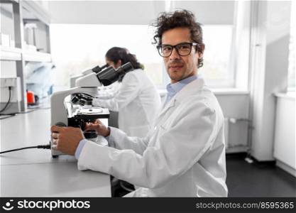 science research, work and people concept - male scientist with microscope working in laboratory. scientist with microscope working in laboratory