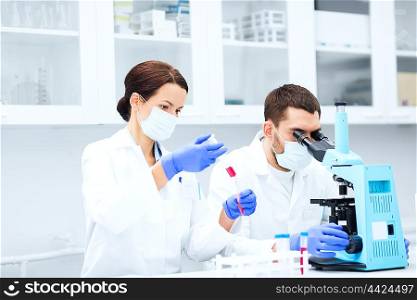 science, technology, biology and people concept - young scientists with pipette, test tube and microscope making research in clinical laboratory