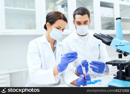 science, technology, biology and people concept - young scientists with pipette, test tube and microscope making research in clinical laboratory