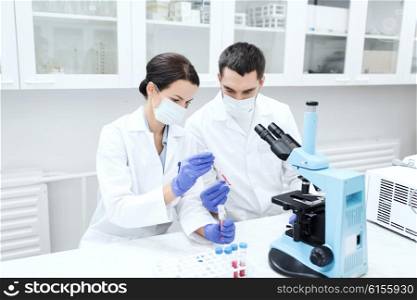 science, technology, biology and people concept - young scientists with pipette, test tube and microscope making research in clinical laboratory