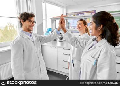 science, work and people concept - international group of happy scientists making high five gesture in laboratory. happy international scientists in laboratory