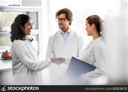 science, work and people concept - international group of happy scientists shaking hands in laboratory. scientists shaking hands in laboratory