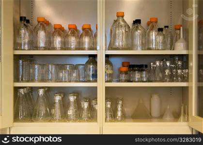 Scientific beakers and bottles in a cabinet.
