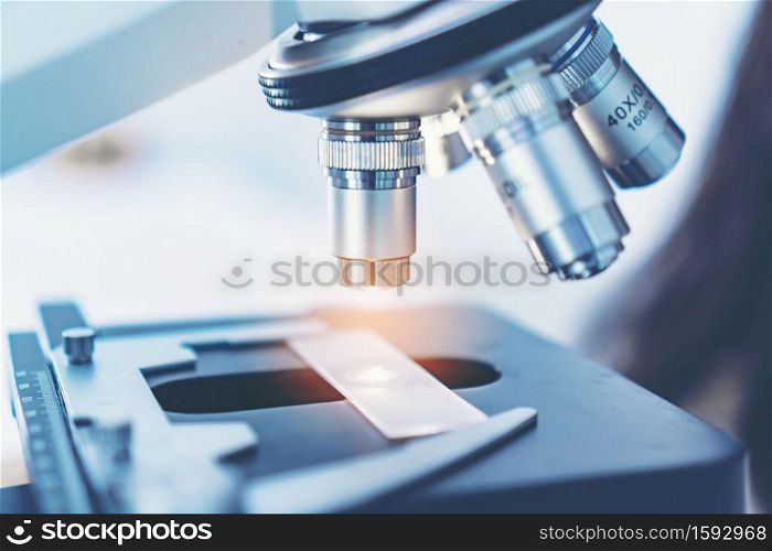 Scientist analyzing microscope slide at laboratory. Young woman technician is examining a histological sample, a biopsy in the laboratory of cancer research