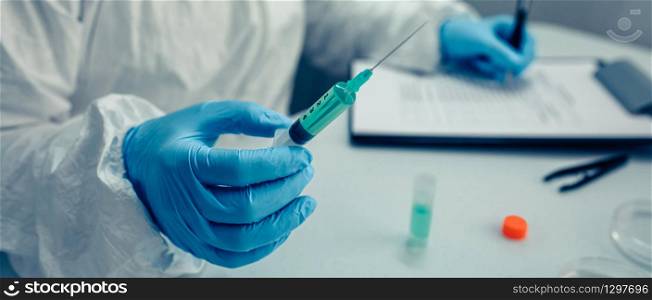 Scientist hand holding a syringe with virus vaccine in the laboratory. Selective focus on vaccine in the foreground