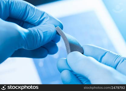 Scientist hand in gloves hold and bend small piece of gray porous foam, new type of material with different properties research concept