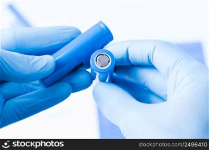 Scientist hold in hand in protective gloves small accumulator battery, new type of rechargeable battery research concept