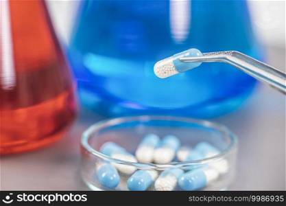 Scientist holding two-colored medicine with tweezers above petri dish. Pharmaceutical research.. Scientist Holding Medicine with Pincers Above Petri Dish