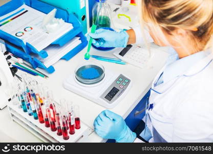 Scientist in gloves measuring weight of blue bulk solid substance in the scientific chemical laboratory