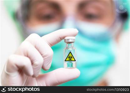 Scientist in protective mask holding sample tube with biohazard sign .. Scientist in protective mask holding sample tube with biohazard sign.