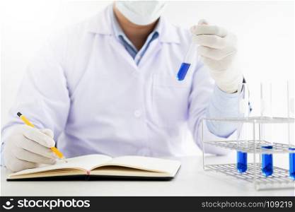 Scientist in white coat holding and examining test tube with reagent making notes of his research in laboratory.