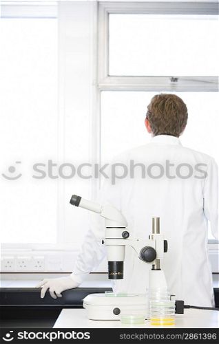 Scientist standing behind microscope in laboratory