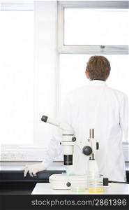 Scientist standing behind microscope in laboratory