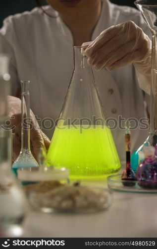 Scientist working with test tubes, flask and other glassware. Woman wears protective goggles