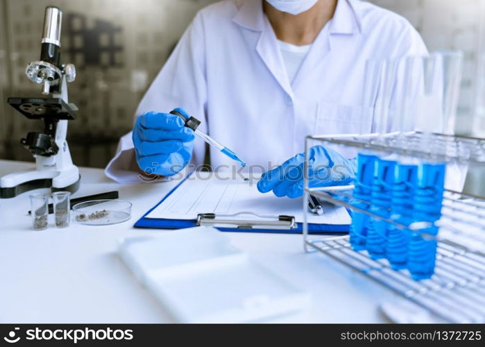 scientists researching in laboratory in white lab coat, gloves analysing, looking at test tubes sample, biotechnology concept.