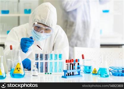Scientists use dropper to drop blood sample to test tube in tube rack to research and develop vaccine for coronavirus covid-19 pandemic with his colleague in background. Medical Science concept.
