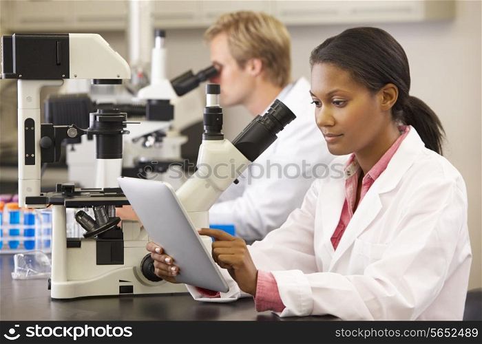Scientists Using Microscopes And Digital Tablet In Laboratory
