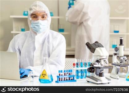 Scientists working in lab using laptop to research and develop vaccine for coronavirus covid-19 pandemic with his colleague in background. Medical Science technology and healthcare concept.
