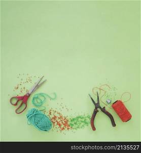 scissor plier wool beads orange yarn spool green background