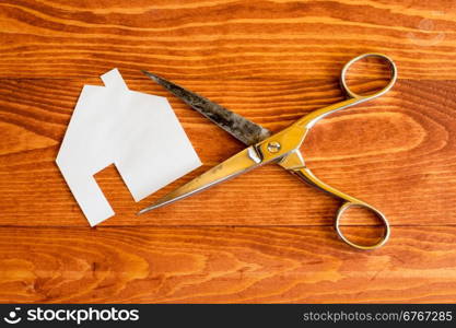 Scissors and house cut out of paper on the wooden background
