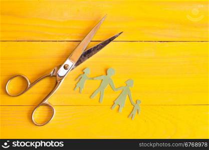 Scissors and paper cut people on the yellow wooden surface