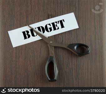 "Scissors cutting the word "Budget" written on a paper strip, over wooden background"
