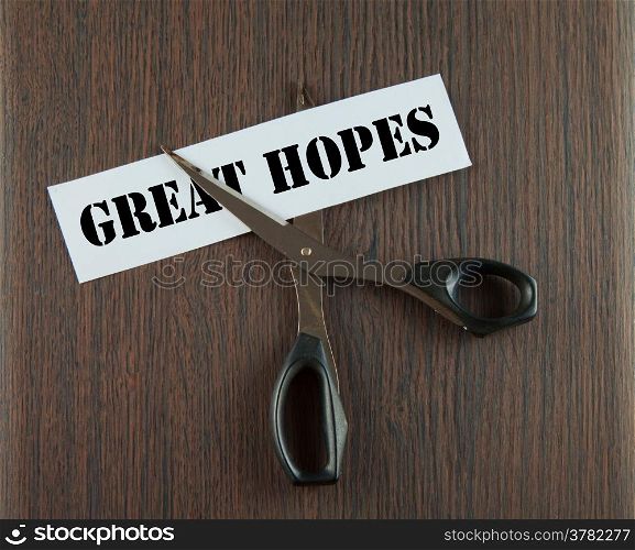 "Scissors cutting the words "Great Hopes" written on a paper strip, over wooden background"