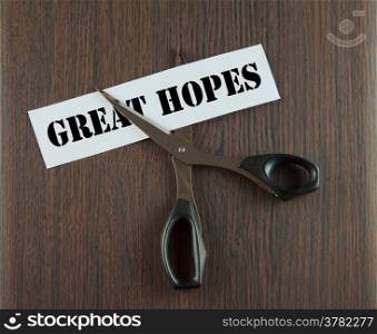 "Scissors cutting the words "Great Hopes" written on a paper strip, over wooden background"