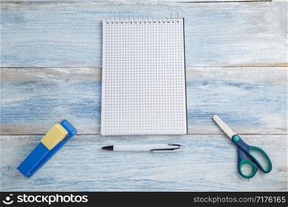 scissors,stapler and notebook with a pen on a blue and white shabby vintage wooden background. the view from the top. Flat lay