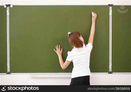 Scoolgirl standing in class near a green blackboard