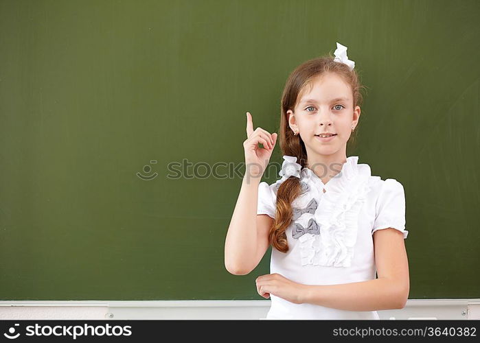 Scoolgirl standing in class near a green blackboard