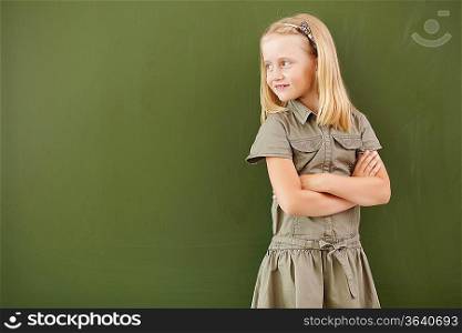 Scoolgirl standing in class near a green blackboard