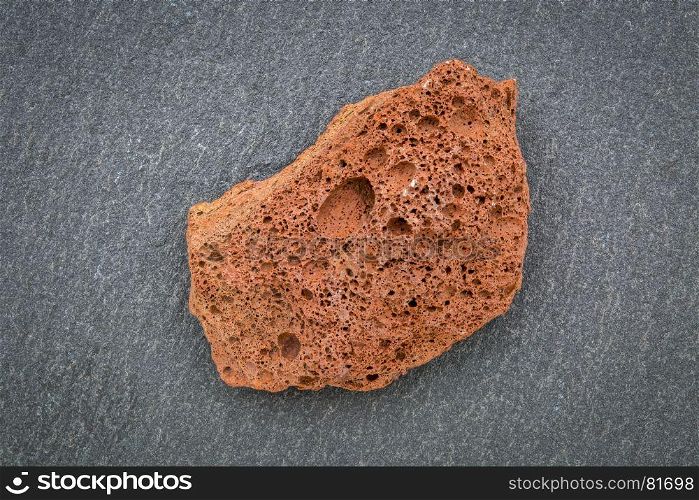 scoria igneous rock sample against gray slate stone, extrusive rock formed from fast-cooling lava blasted out of volcano