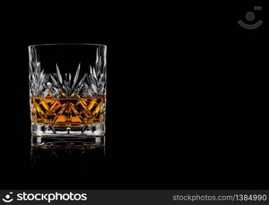 Scotch whiskey in crystal elegant glass on black background with reflection.Space for text