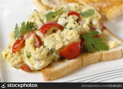 Scrambled egg on toast with cherry tomatoes, parsley and pepper. Cooking in a bain marie allows the tomatoes to be incorporated rather than curdling. close-up.