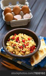 Scrambled eggs made with red bell pepper and green onion in rustic bowl with toasted bread on the side and eggs in the back, photographed with natural light (Selective Focus, Focus one third into the scrambled eggs)
