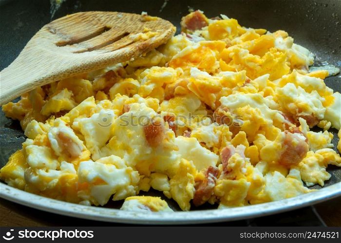 Scrambled eggs with bacon in a pan, close up