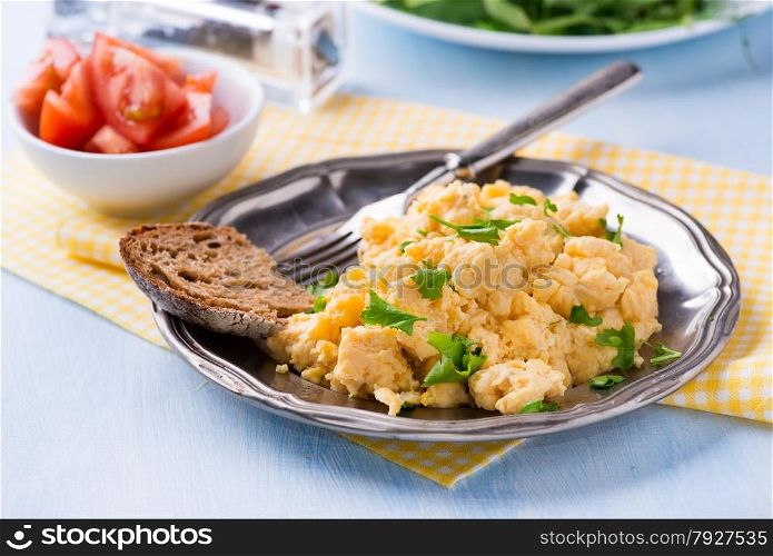 Scrambled eggs with fresh parsley on vintage metal plate, rye bread and tomato, selective focus