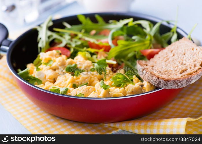 Scrambled eggs with fresh tomato and arugula salad in frying pan, selective focus