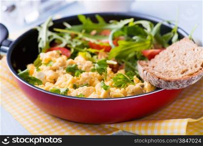 Scrambled eggs with fresh tomato and arugula salad in frying pan, selective focus