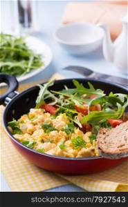 Scrambled eggs with fresh tomato and arugula salad in frying pan, selective focus