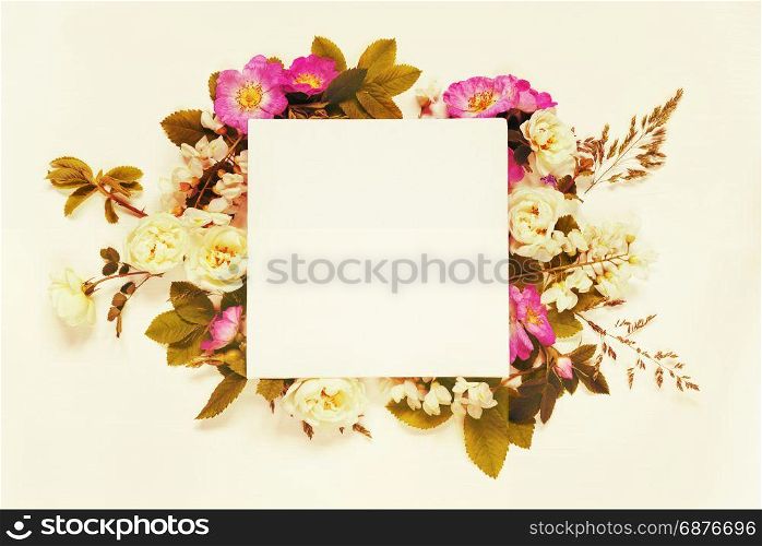 Scrapbook page of wedding or family photo album, frame with wild rose, white flowers and green leaves on light wooden background; top view, flat lay, overhead view. Mocap. Toned image