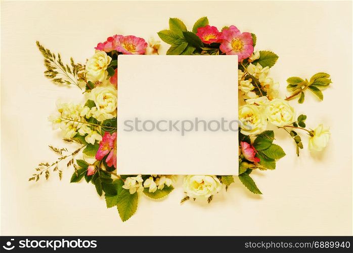 Scrapbook page of wedding or family photo album, frame with wild rose, white flowers and green leaves on light wooden background; top view, flat lay, overhead view, toned image