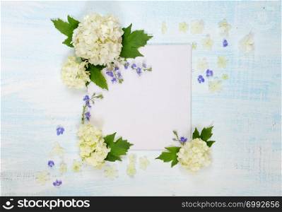 Scrapbooking page of wedding or family photo album, frame with fresh white and blue flowers and green leaves and flower petals on light wooden background; top view, flat lay, overhead view