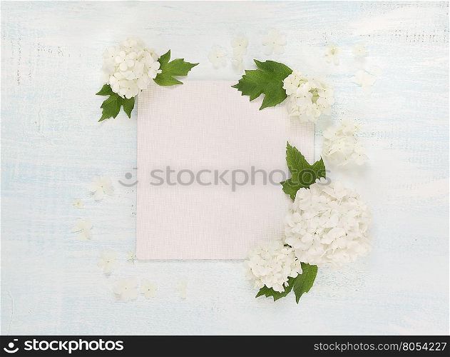 Scrapbooking page of wedding or family photo album, frame with fresh white flowers and green leaves on light wooden background; top view, flat lay, overhead view