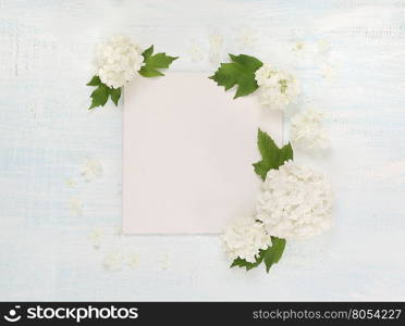 Scrapbooking page of wedding or family photo album, frame with fresh white flowers and green leaves on light wooden background; top view, flat lay, overhead view