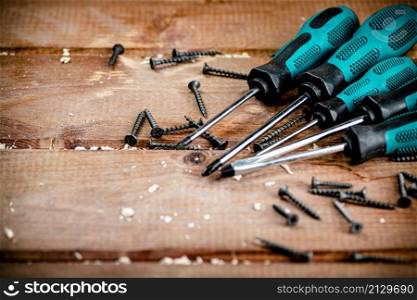 Screwdriver with a bunch of self-tapping screws. On a wooden background. High quality photo. Screwdriver with a bunch of self-tapping screws.