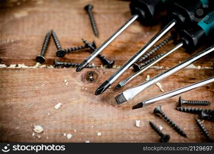 Screwdriver with a bunch of self-tapping screws. On a wooden background. High quality photo. Screwdriver with a bunch of self-tapping screws.