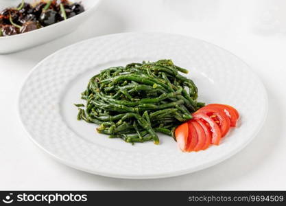 Sea beans with cold tomatoes on a white porcelain plate