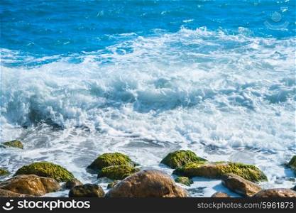 Sea coast with stones, surfing wave on the background
